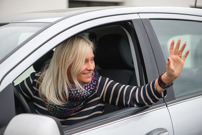 Woman waving hand while sitting in car