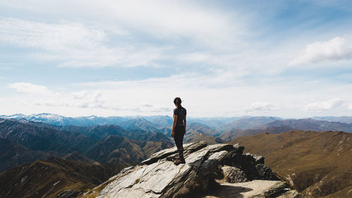 Man standing on rock looking at mountains against sky