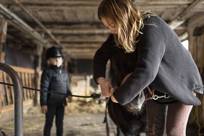 Mother with daughter preparing pony for ride