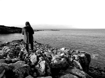 Rear view of girl standing on rock against sea