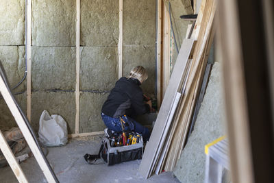 Female technician with drill machine drilling on wall by tool box