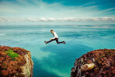 Man on rock by sea against sky