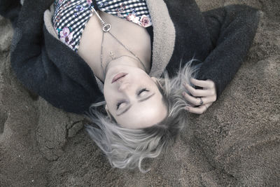 High angle view of beautiful young woman wearing chain with key pendant while lying on sand at beach