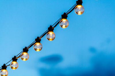Low angle view of illuminated light bulbs against blue sky
