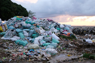 Stack of stones by garbage on land against sky