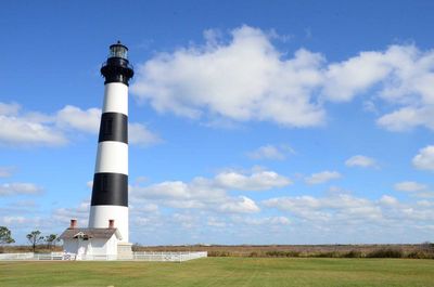 Lighthouse on landscape against cloudy sky