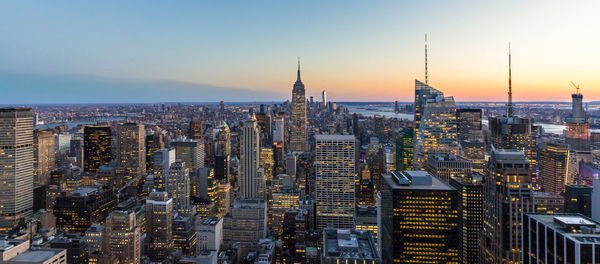 Empire state building amidst cityscape at manhattan during sunset