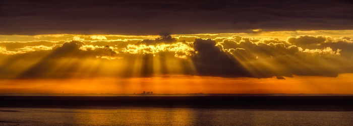 Sunlight streaming through clouds over sea during sunset