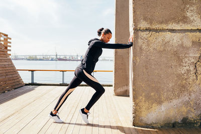 Full length of woman exercising on boardwalk during sunny day