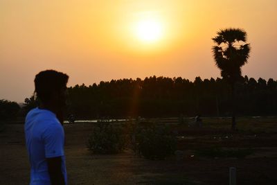 Rear view of silhouette man standing by trees against sky during sunset