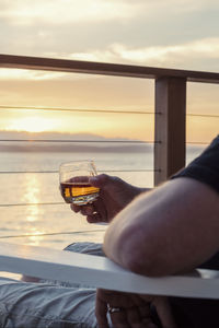 Close-up of hand holding drink at sunset