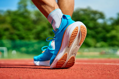 Athlete wearing bright blue running shoes on red stadium track during training