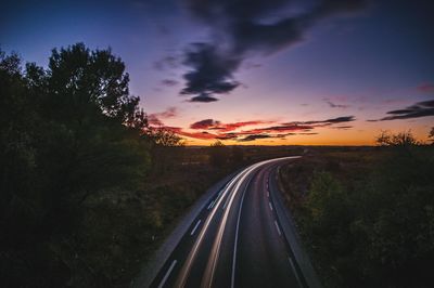 Road amidst trees against sky during sunset