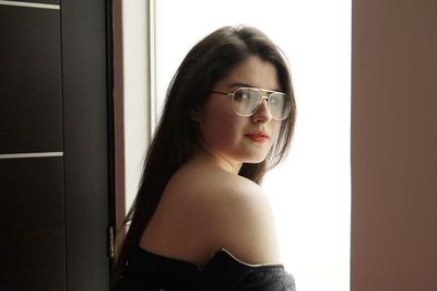 Portrait of young woman standing by window at home