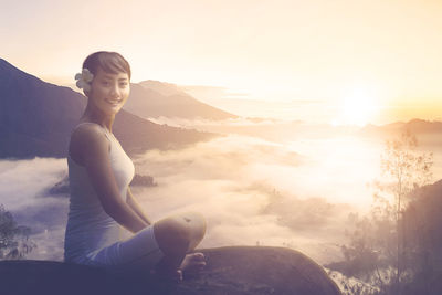 Young woman sitting on mountain against sky during sunset
