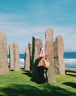 Woman standing on rock by sea against sky
