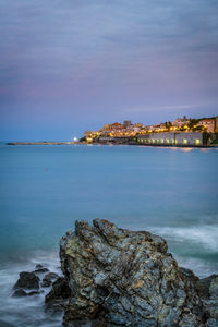 Rock at sea shore against sky during sunrise