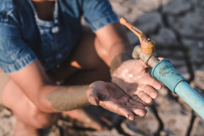 Boy with hands cupped crouching under empty faucet