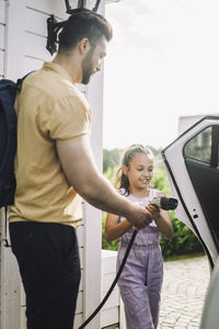 Side view of father teaching daughter to charge electric car