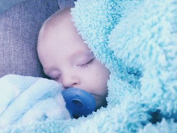 Close-up of baby boy sucking pacifier while sleeping on bed