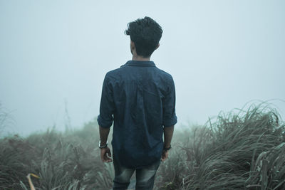 Rear view of man standing on mountain during foggy weather