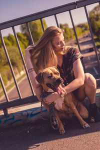 Young woman embracing dog while sitting on footbridge