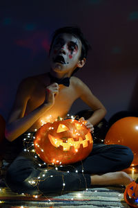 Close-up of woman holding pumpkin while sitting on illuminated during halloween