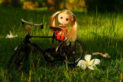 Doll and artificial bicycle on grassy field