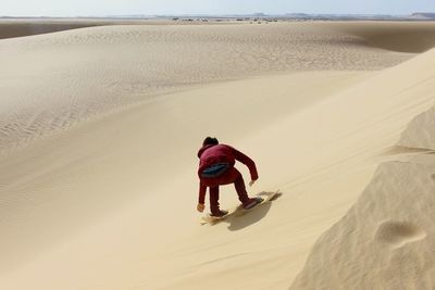 Rear view of man climbing on tire tracks on sand