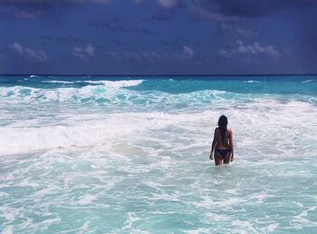 Rear view of woman standing at beach against sky