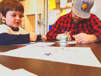 Father and son drawing with crayons in papers at home
