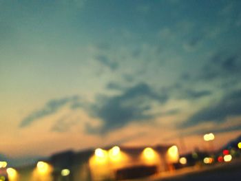 Defocused image of illuminated lights against sky at sunset