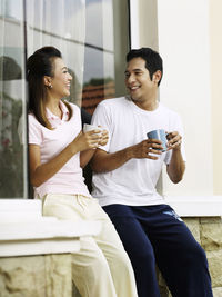 Smiling couple talking while having coffee against wall
