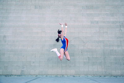 Full length of cheerful female gymnast in leotard jumping against wall