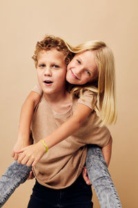 Portrait of smiling sibling playing against beige background