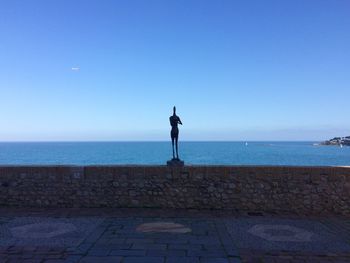 Man standing by sea against clear blue sky