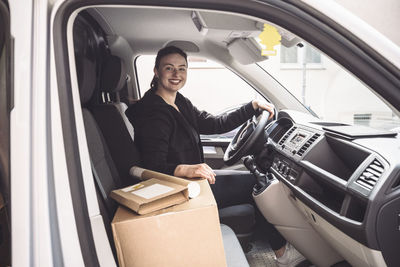 Portrait of smiling delivery woman with package sitting in truck