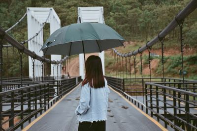 Rear view of woman with umbrella standing on footbridge