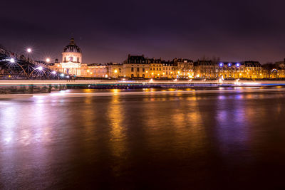 Illuminated buildings by river against sky at night