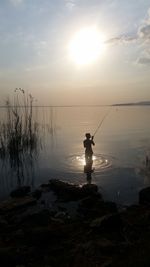 Silhouette of man on sea against sky during sunset