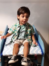 Cute boy sitting over shelf against wall