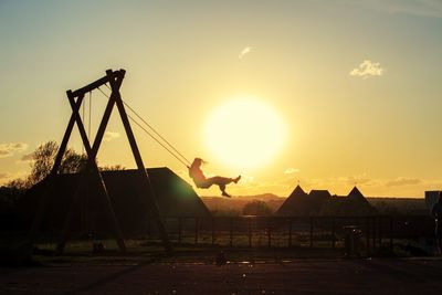Silhouette cranes on field against sky during sunset
