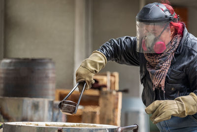 A female raku technician unloads ceramic ware with tongs, gloves and protective helmet from a kiln