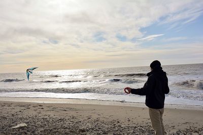 Man flying kite while standing at beach against sky