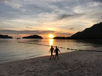 Silhouette people on beach against sky during sunset