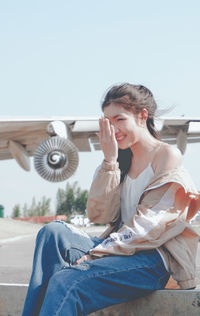 Young woman sitting outdoors against clear sky