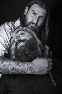 Portrait of barber cutting beard of man against black background