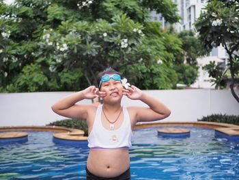 Woman gesturing peace sign in swimming pool against trees