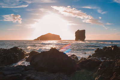 Rocks on beach against sky during sunset