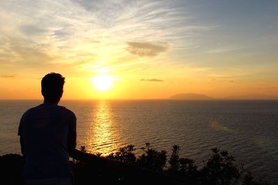 Rear view of man looking at sea against sky during sunset